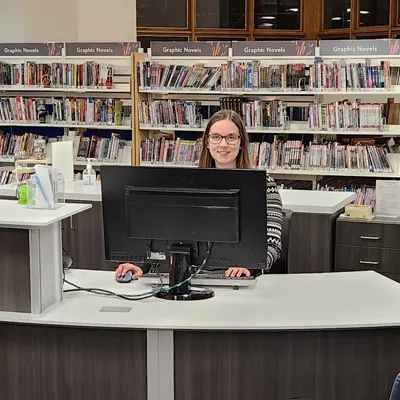 Smiling librarian sitting at the Adult Desk, ready to help