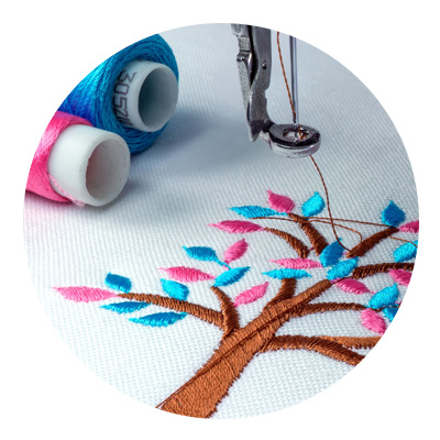 Closeup of a tree with pink and turquoise leaves. Embroidery needle and spools of thread are visible